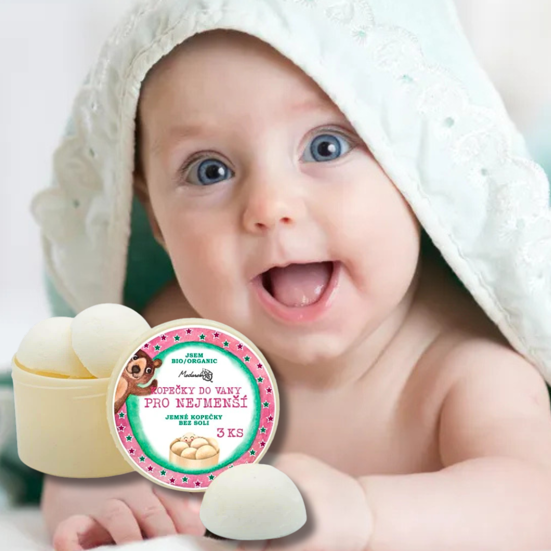 Gentle bath melts “Kopečky do vany pro nejmenší” in front of a smiling baby wrapped in a towel.